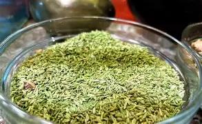 Fennel seeds (sounf) in a rustic bowl, showcasing their fresh green color and elongated shape.